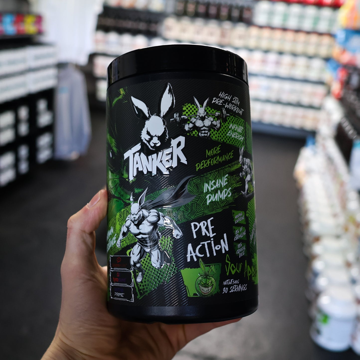 Hand holding a 'Tanker' pre-action pre workout supplement container in a store setting
