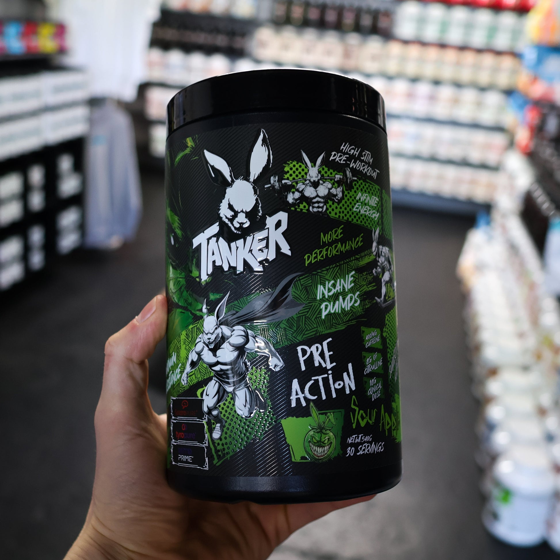 Hand holding a 'Tanker' pre-action pre workout supplement container in a store setting