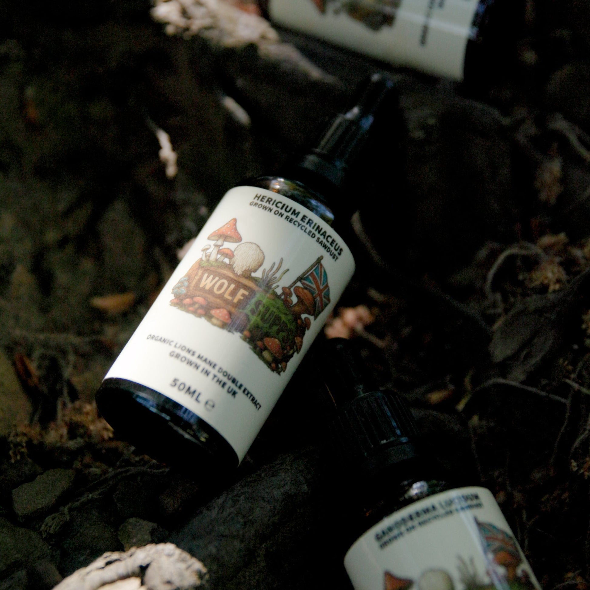 Two small black dropper bottles with white labels featuring woodland illustrations, placed on dark forest bark and leaves. One label clearly reads 'WOLF' and 'SERVUM ENIMACI'; another partially visible label at the bottom right reads 'BARKERMA LUPUS'.