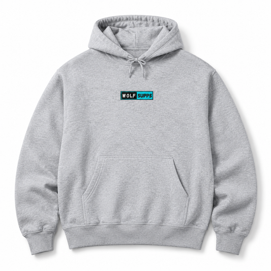 A light gray heather pullover hoodie with a small rectangular chest logo that reads 'WOLF SUPPS' in white text on a teal and black background. The hoodie features a drawstring hood, a front kangaroo pocket, and ribbed cuffs and hem, shown against a plain white background.
