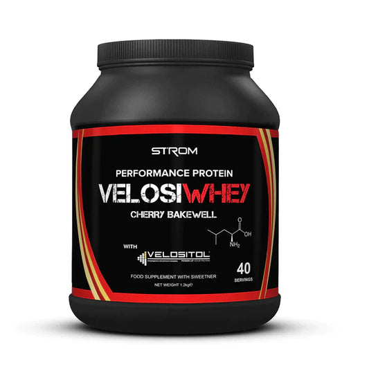 A black tub of Strom Velosi Whey protein powder in Cherry Bakewell flavor, featuring a black label with red and gold accents and white text, set against a plain white background.